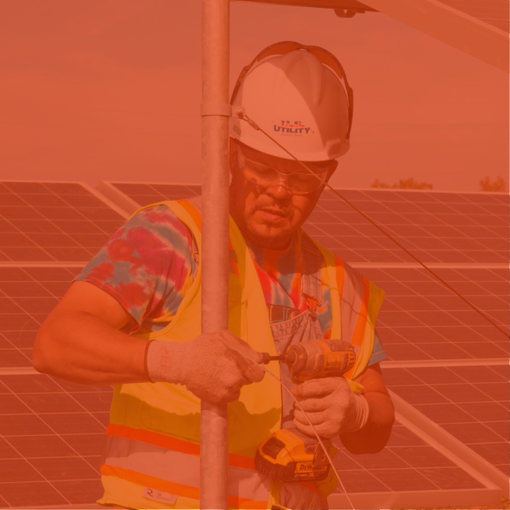 A photo of someone working on solar panels with a hardhat on and drill in hand.